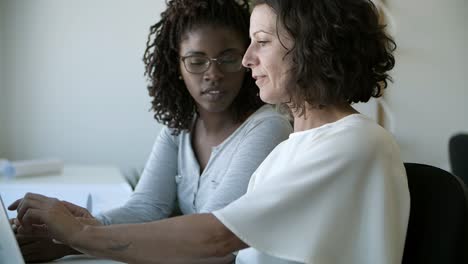 two confident women talking while working with laptop