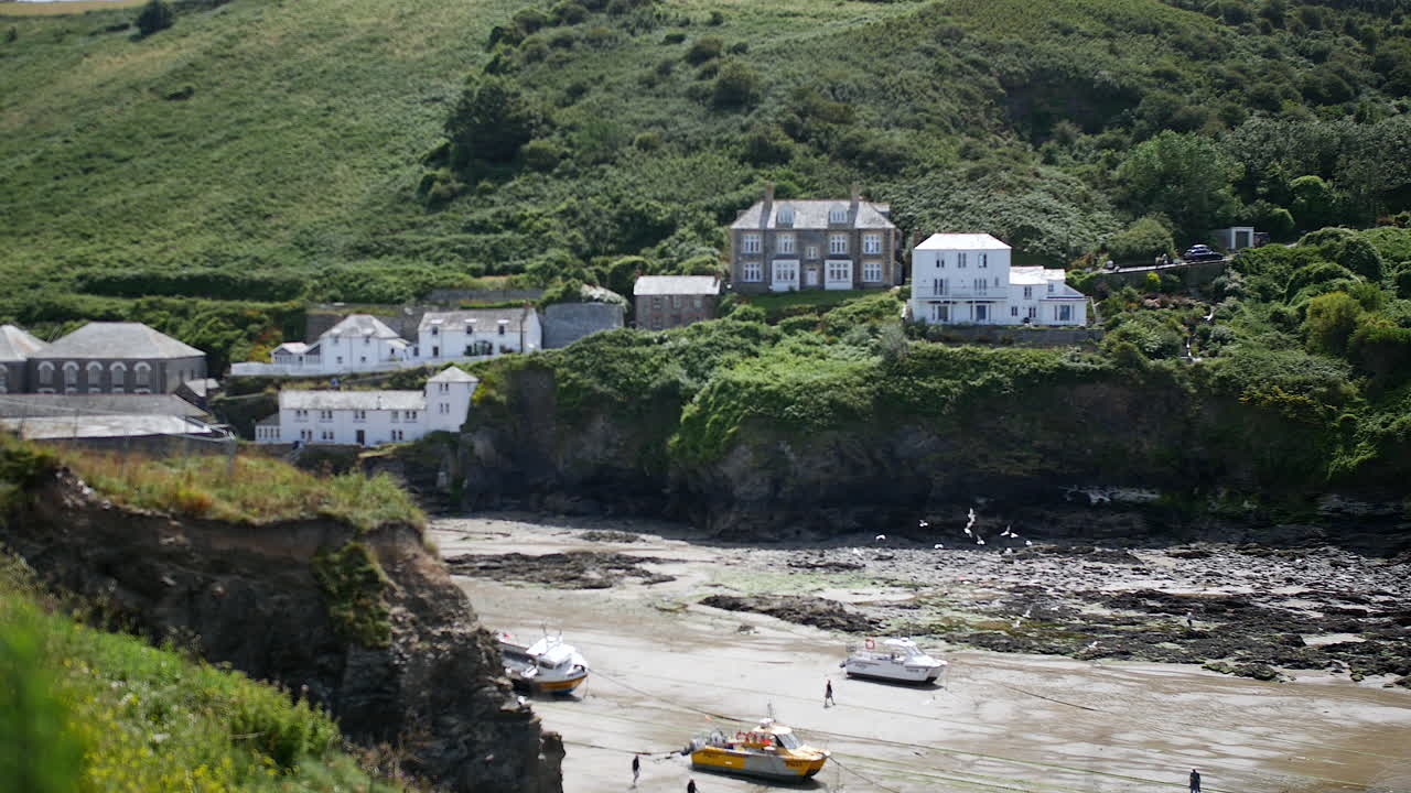 A village with white cottages and stone buildings is sitting above a tidal inlet in Cornwall, capturing the coastal charm of Port Isaac and the setting of Portwenn