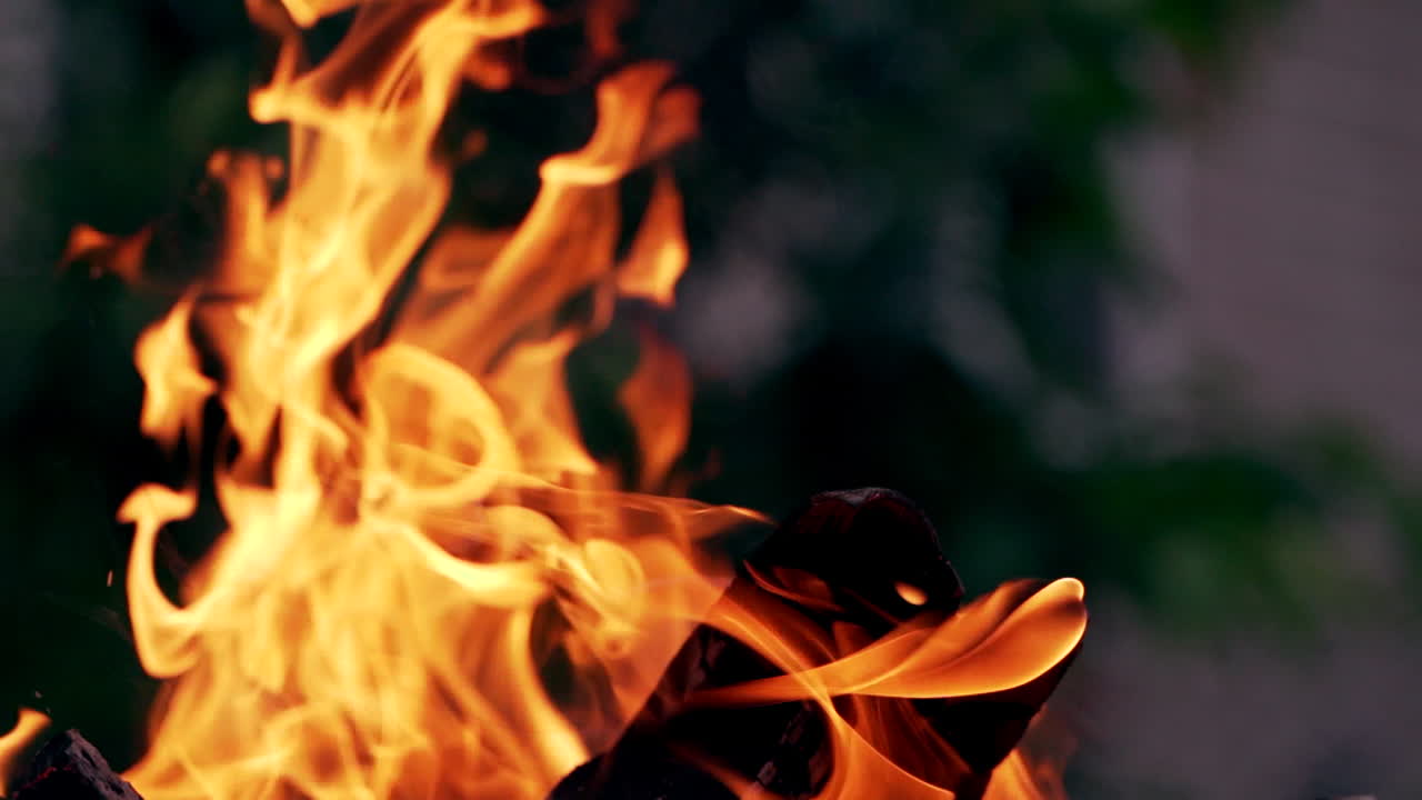 Orange flame on smoldered logs on blurred background. Bright campfire in the street in the evening in summer. Close-up.