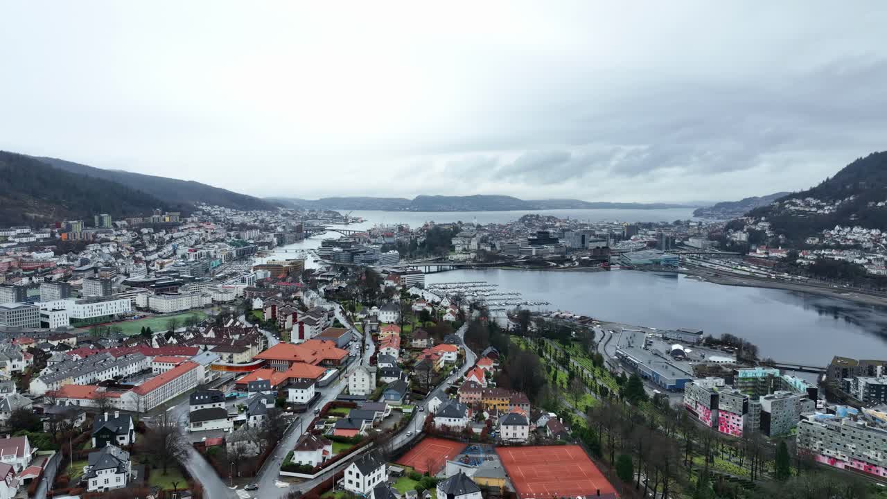Aerial descent over Bergen city center, revealing Byfjorden, Lungegaardsvann, and Puddefjord. Wide panoramic urban view in misty winter conditions