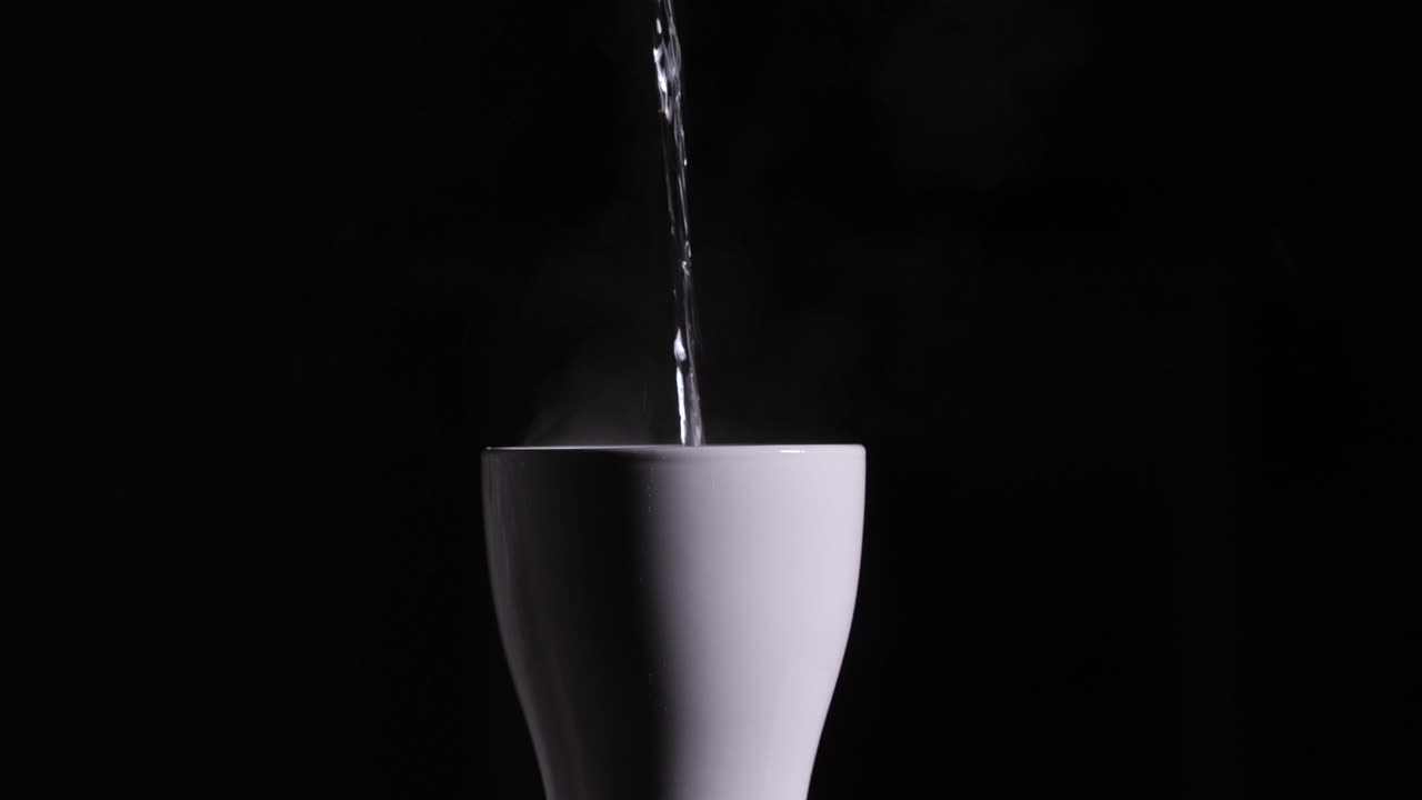 Acqua bollente viene versata in una tazza o boccale di ceramica bianca su sfondo nero