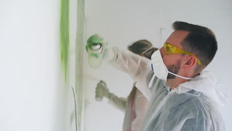 guy and girl in protective suits paint wall with sprays