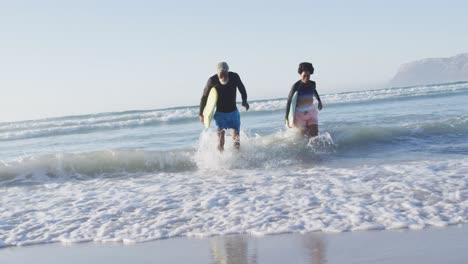 happy african american couple running with surfboards on sunny beach