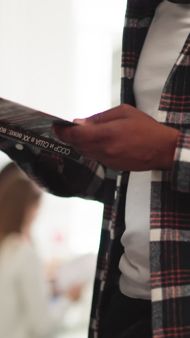 hombre negro sostiene un libro en la biblioteca de la universidad de cerca. lector absorto lee el libro de texto de pie cerca del estante en la librería. estudiante elige literatura científica