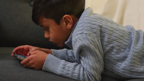 young boy lying on sofa at home playing game or streaming onto handheld gaming device 6