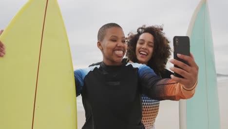 felices amigas afroamericanas en la playa sosteniendo tablas de surf tomando selfies