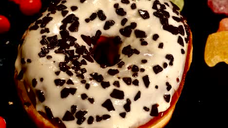 white glazed donut with chocolate, icing or sprinkles, striped caramel candies, colorful dragee with raisins or peanuts inside on black background