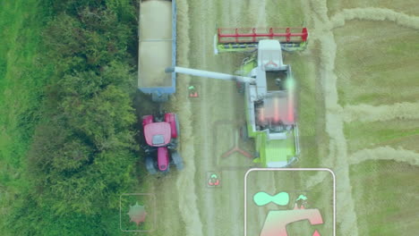 unloading grain, combine harvester filling tractor trailer on farm from aerial view