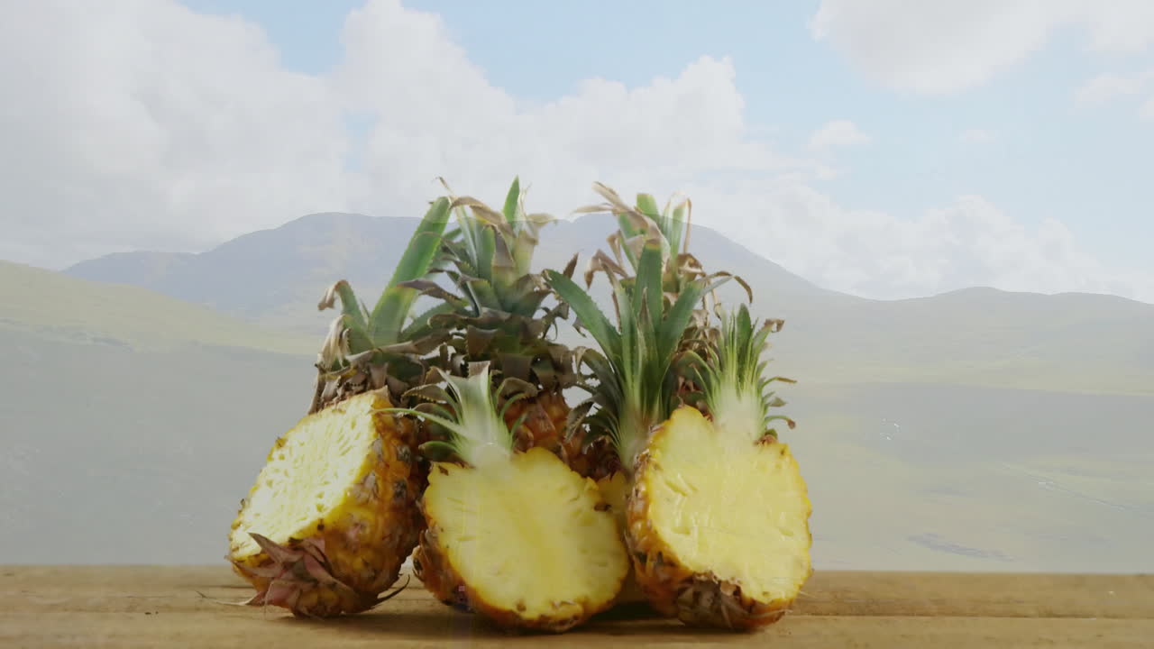 Sliced pineapples on wooden surface, mountain landscape visible in background