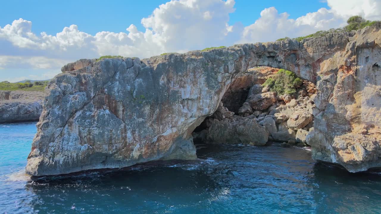 Experience the breathtaking Cala Varques rock formation surrounded by turquoise waters and lush landscapes. Enjoy the serene beauty of Majorca and its natural wonders on a perfect sunny day.