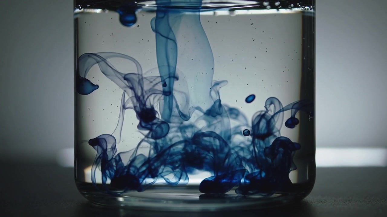 Dropping blue dye droplet forming descending plume inside glass jar on dark surface, showing mixing