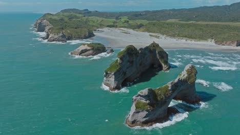 panorámica aérea que gira alrededor de formaciones rocosas costeras únicas en el popular destino turístico de la playa de wharariki en el cabo de despedida en nelson, isla sur de nueva zelanda aotearoa