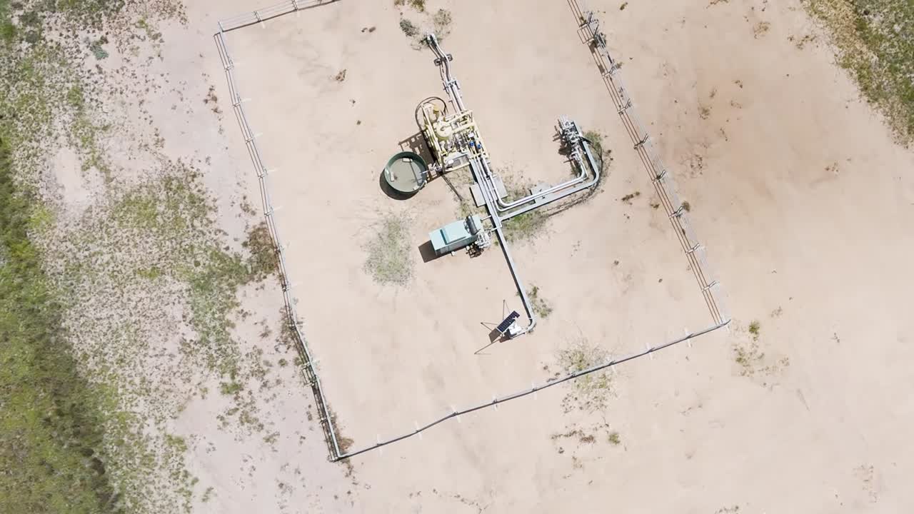 Top-down view of a single gas well surrounded by sparse vegetation and sandy terrain.