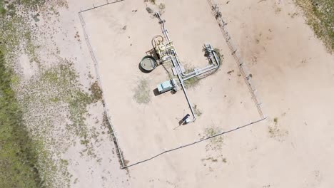 Top-down view of a single gas well surrounded by sparse vegetation and sandy terrain.