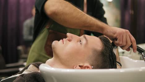 vista de cerca de un joven que se lava el cabello y un barbero irreconocible en un tiro de barbero