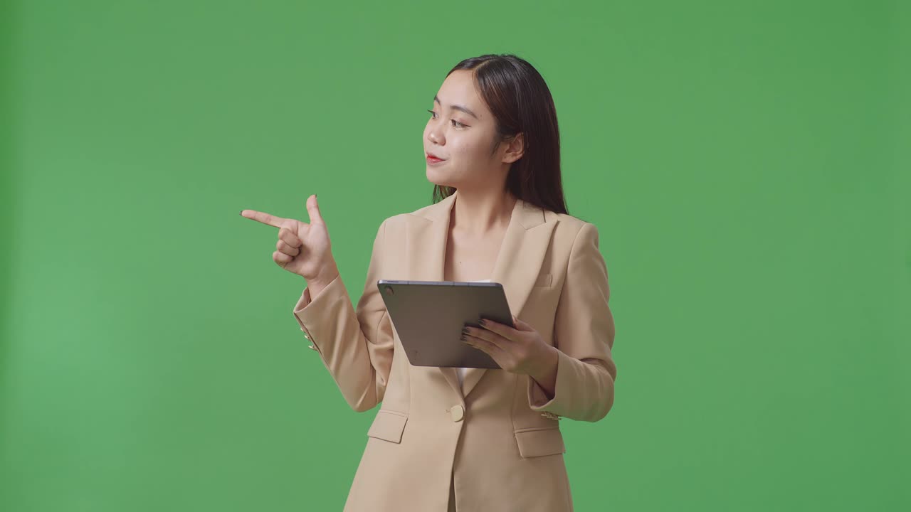 アジアのビジネスウーマンがタブレットを使用しスタジオの緑色のスクリーン背景に横を指しています