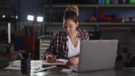 mecánica tomando notas y usando una computadora portátil en una estación de servicio de automóviles