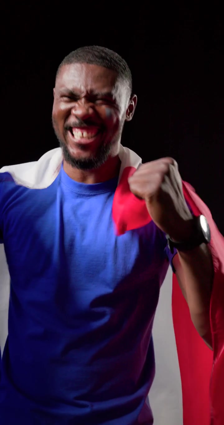 Vídeo vertical: Homem afro-americano pegando uma bandeira tricolor drapeada e agitando, aplaudindo em estúdio.
