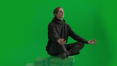 young man meditating in a green screen studio