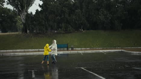 una adolescente feliz en una chaqueta amarilla bailando con su madre en una jaqueta blanca durante la lluvia en el parque