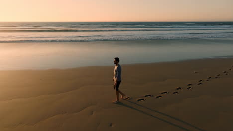a man walking on a beach at sunset, leaving footprints in the sand