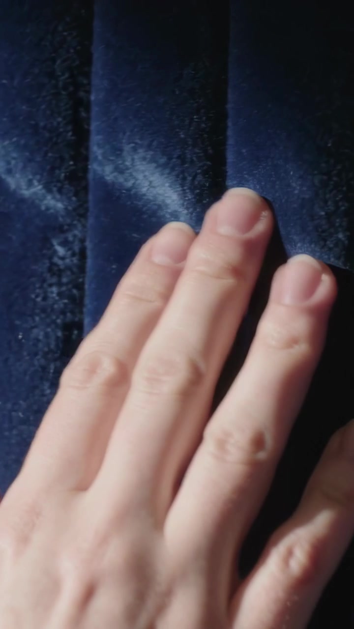 Vertical video: Reaching left hand stroking velvet curtain at home, showing nap streaks, copy space