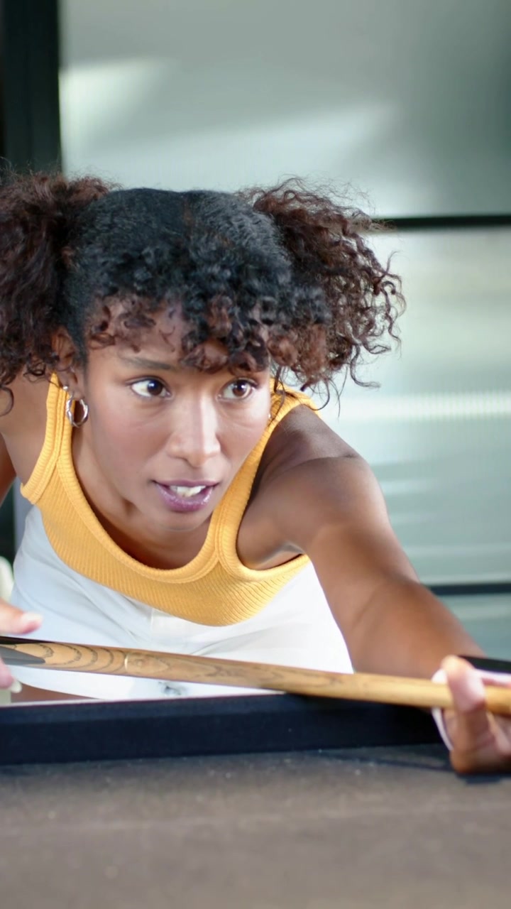 Woman approaching pool table, leaning, aligning cue, executing shot, standing smiling for leisure