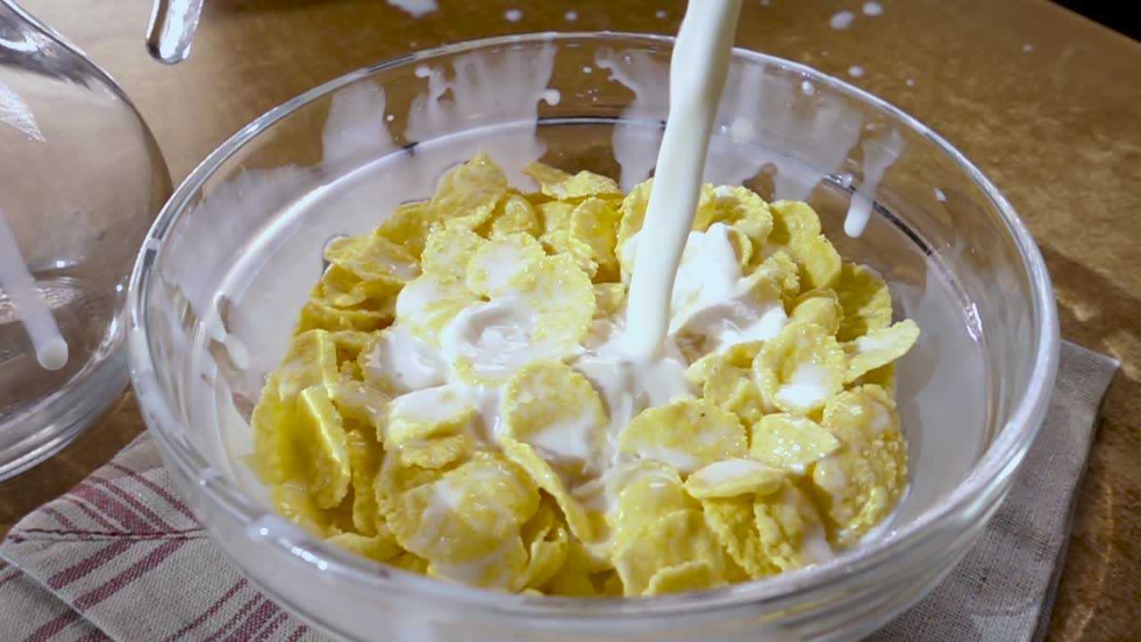 Knusprige gelbe Cornflakes in die Schale für ein köstliches Frühstück mit Milch am Morgen. Zeitlupe mit rotierender Kamerafahrt