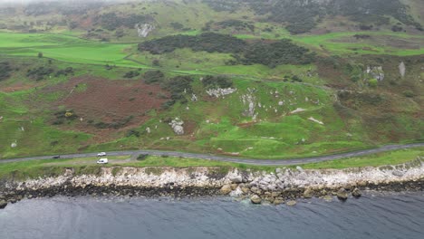 aerial panning view over the idyllic rocky coast road right on the sea with moving cars during an adventurous trip near glenarm town in northern ireland