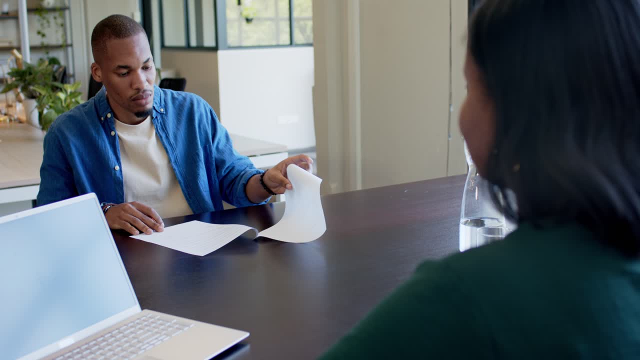 African American team watching man writing and presenting papers with pen laptop after seeing stack