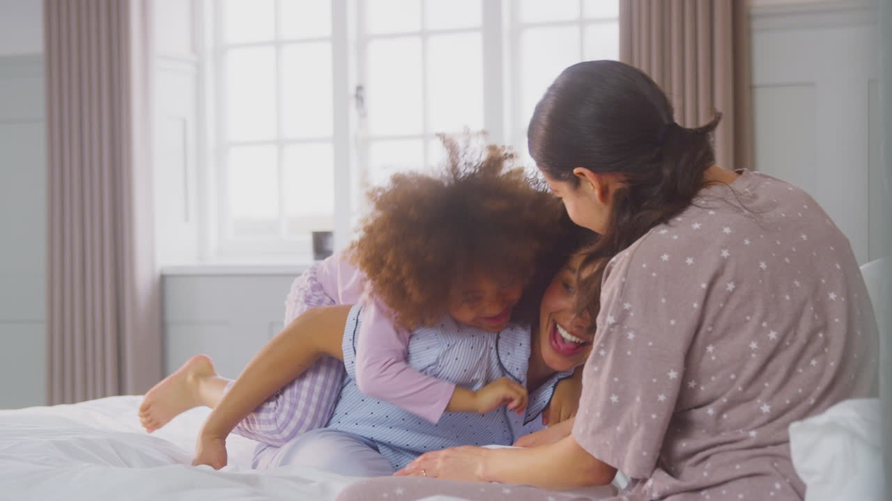 familia con dos madres con pijama jugando en la cama en casa con su hija