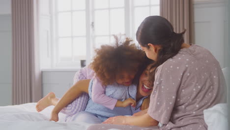 family with two mums wearing pyjamas playing on bed at home with daughter