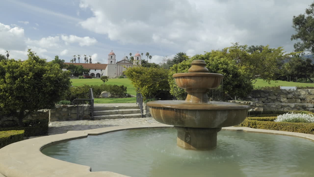 time lapse dolly shot de nubes pasando sobre la misión santa barbara frente a la fuente del jardín de rosas en santa barbara california