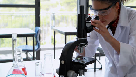 schoolgirl experimenting on microscope in laboratory