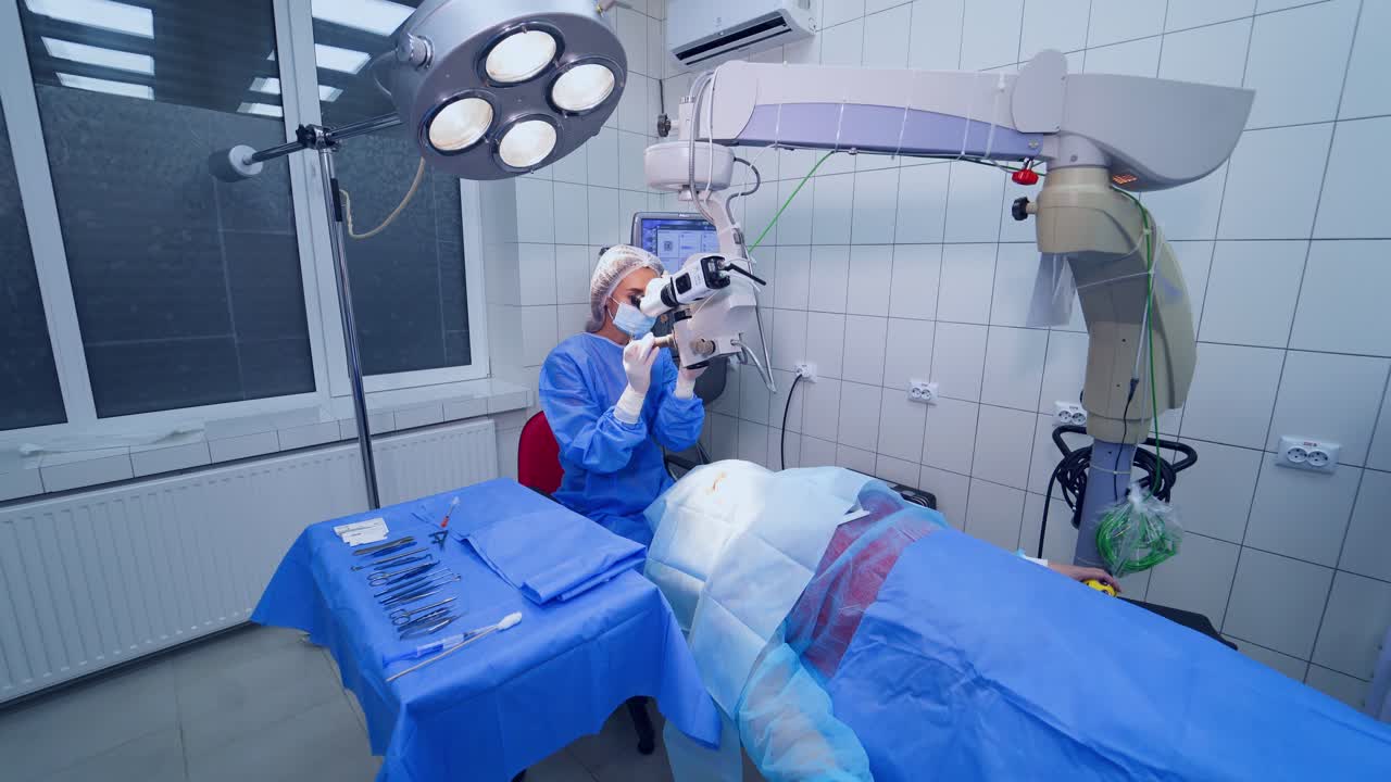 Doctor in medical uniform during operation on the contemporary equipment background in clinic. Female surgeon treating patient's eyes with the microscope.