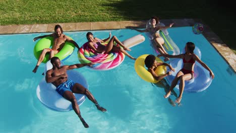 Diverse-group-of-friends-having-fun-playing-on-inflatables-in-swimming-pool