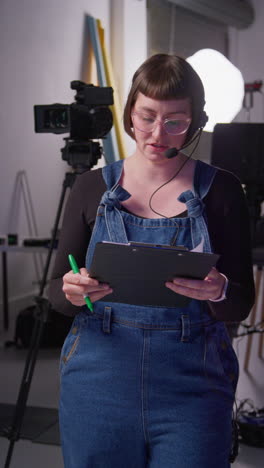 vertical video of female film production assistant with headset and script on movie or video shoot in studio