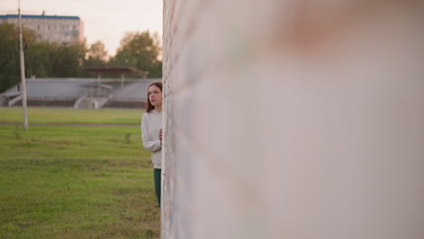 woman hides behind wall of building. young woman checks behind building for spending time alone. depressed hermit woman avoids crowds during walk