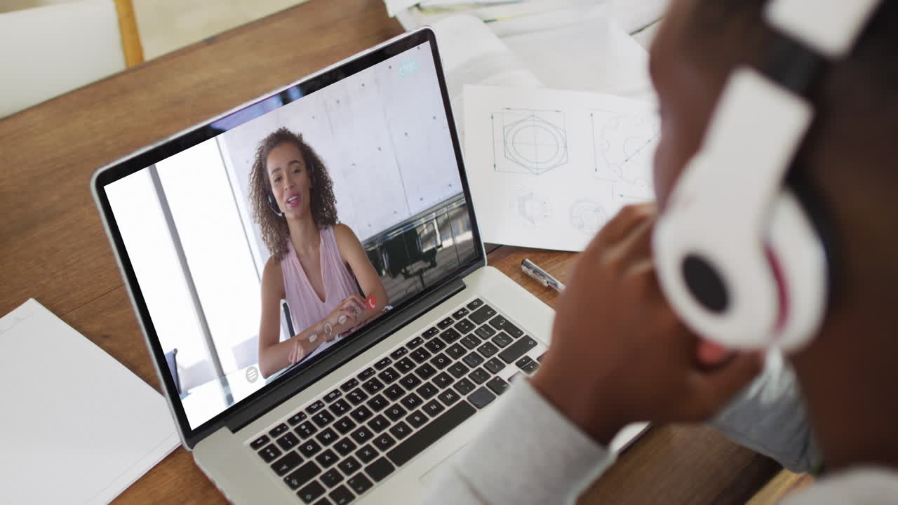 African american male college student holding notes while having a video call on laptop at home