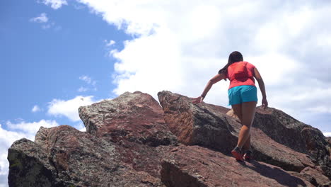 mujer joven escalando en la cima de la roca por encima de las nubes y el cielo en un día soleado de verano a cámara lenta de fotograma completo