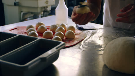 Male-chef-applying-poppy-seeds-on-rolled-dough-balls-4k