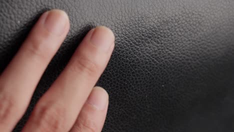 fingers of hand touching gently black leather sleek textured surface, close up