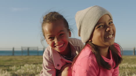 close up portrait of happy mixed race girls sitting playing laughing enjoying seaside park