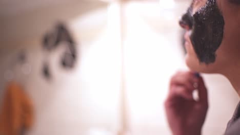 joven mujer caucásica aplicando mascarilla de belleza negra en su cara en casa