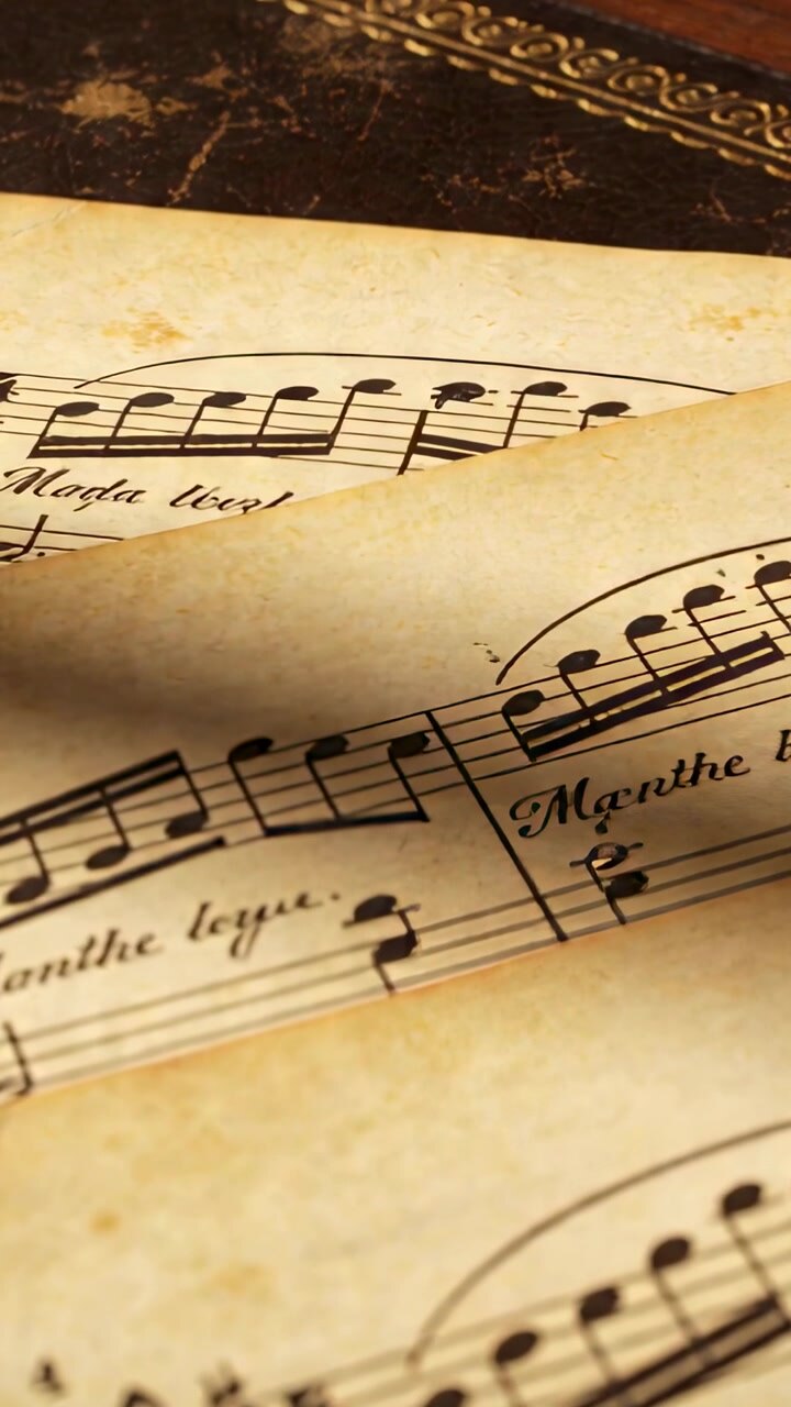 Vertical video: Shifting from draft, aged sheet music curling on desk, revealing staves, gold folio