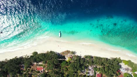 Isla-En-El-Caribe---Barco-Atracado-En-La-Orilla-De-Arena-Blanca-De-Una-Isla-Exuberante-Con-Arrecifes-De-Coral-Vistos-A-Través-Del-Agua-Azul-Clara-Del-Océano---Un-Hermoso-Destino-Turístico---Tiro-Aéreo