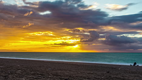 vista estática de la puesta de sol sobre el cielo dorado sobre el mar en timelapse sobre la playa de arena