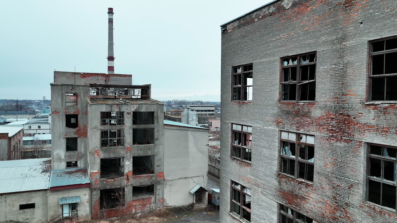 Damaged ruins of past big plant. Forlorn wrecked emptied buildings with no windows and old brick walls. Blue clear sky at the background.
