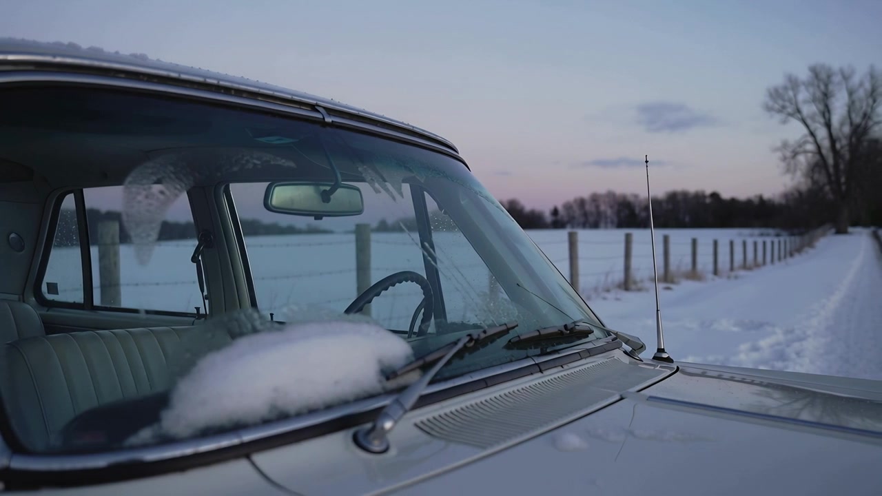 Pulling camera revealing left vintage car on snowy road showing frosted windshield and snow mound