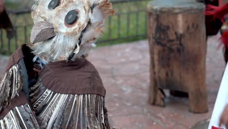 extreme closeup of a mayan or aztec dancer in a bird costume with feathers and large orange headdress that looks like an owl